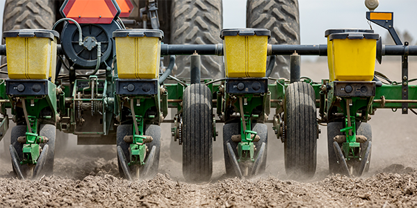 Closeup of tractor and planter in farm field planting corn or soybeans seed in dry, dusty soil during spring season